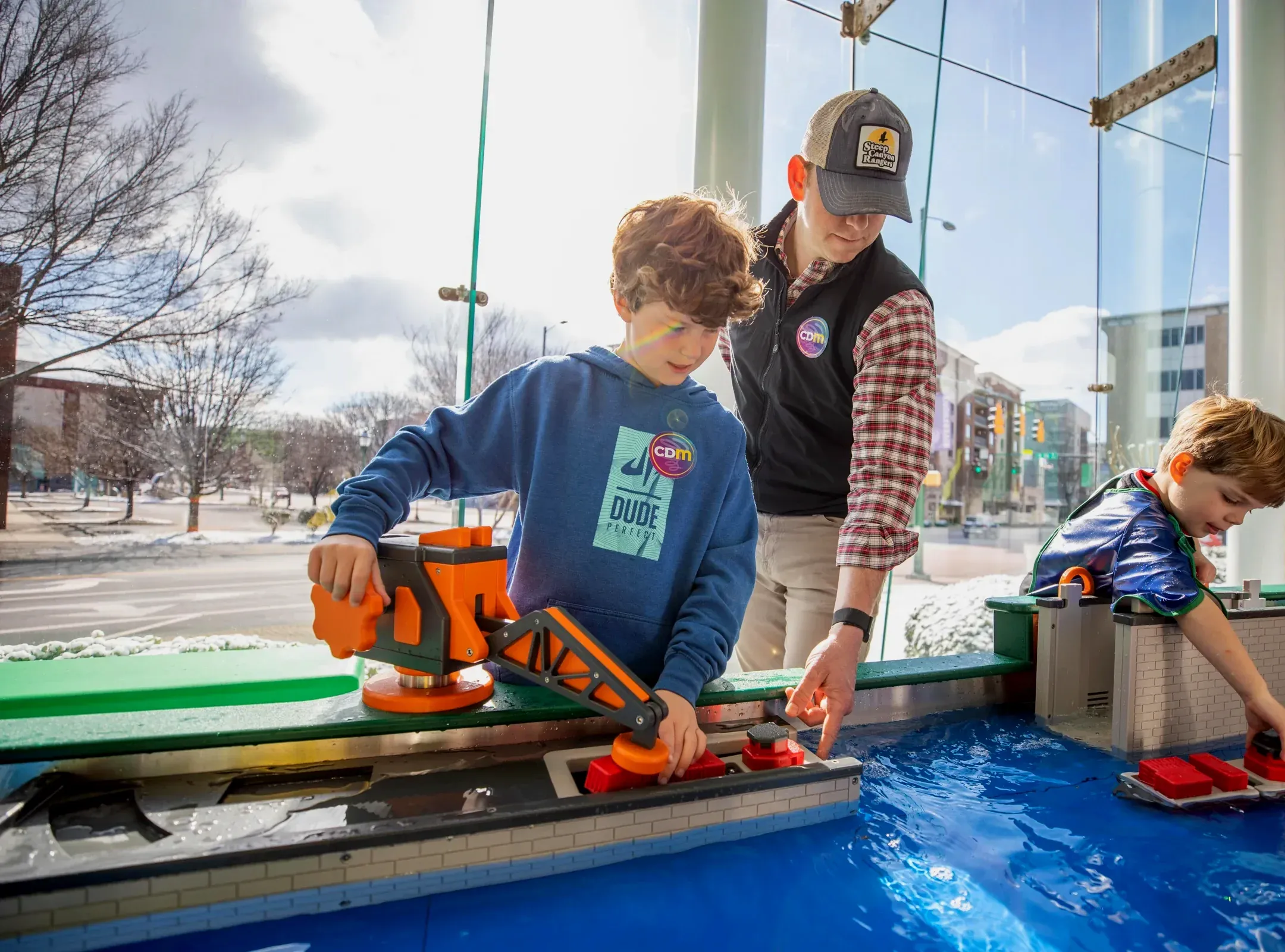 A boy steers a toy boat through the RiverPlay water table on the museum's rooftop, with downtown Chattanooga behind the glass.