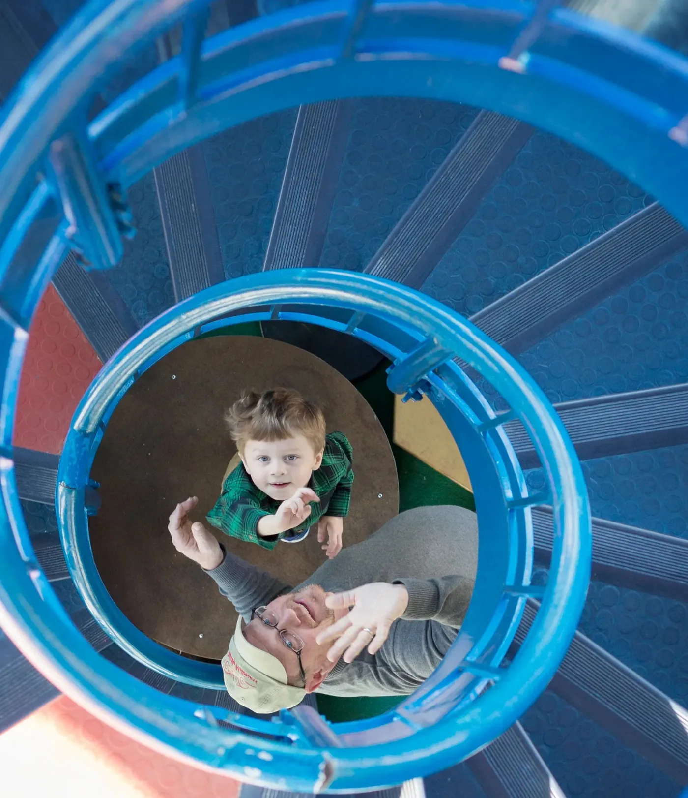 A boy waves down from the Tower's blue spiral climb while an adult looks up from below.