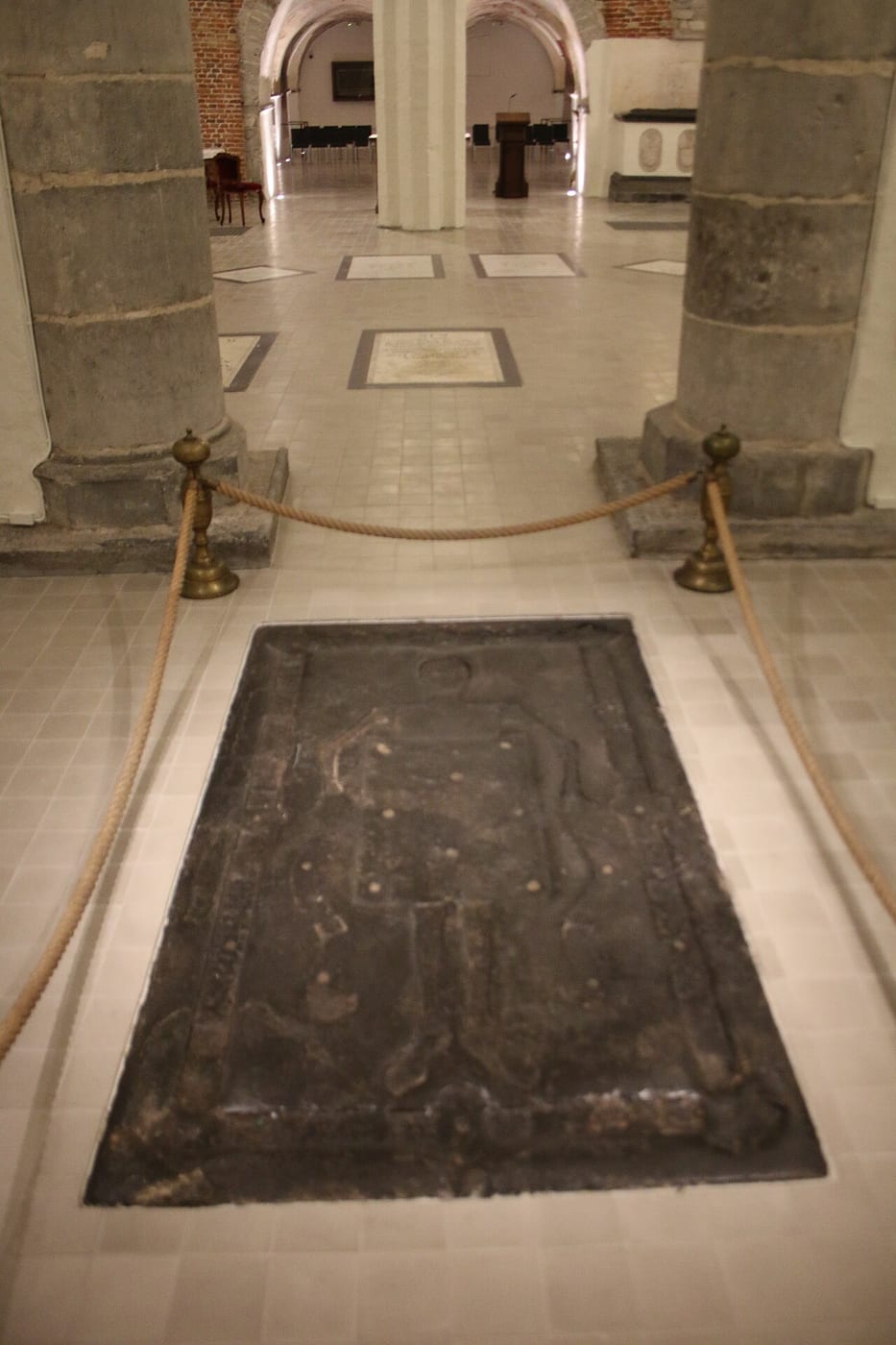 Hubert van Eyck’s worn tombstone in the crypt floor of Saint Bavo’s Cathedral, behind a rope barrier.