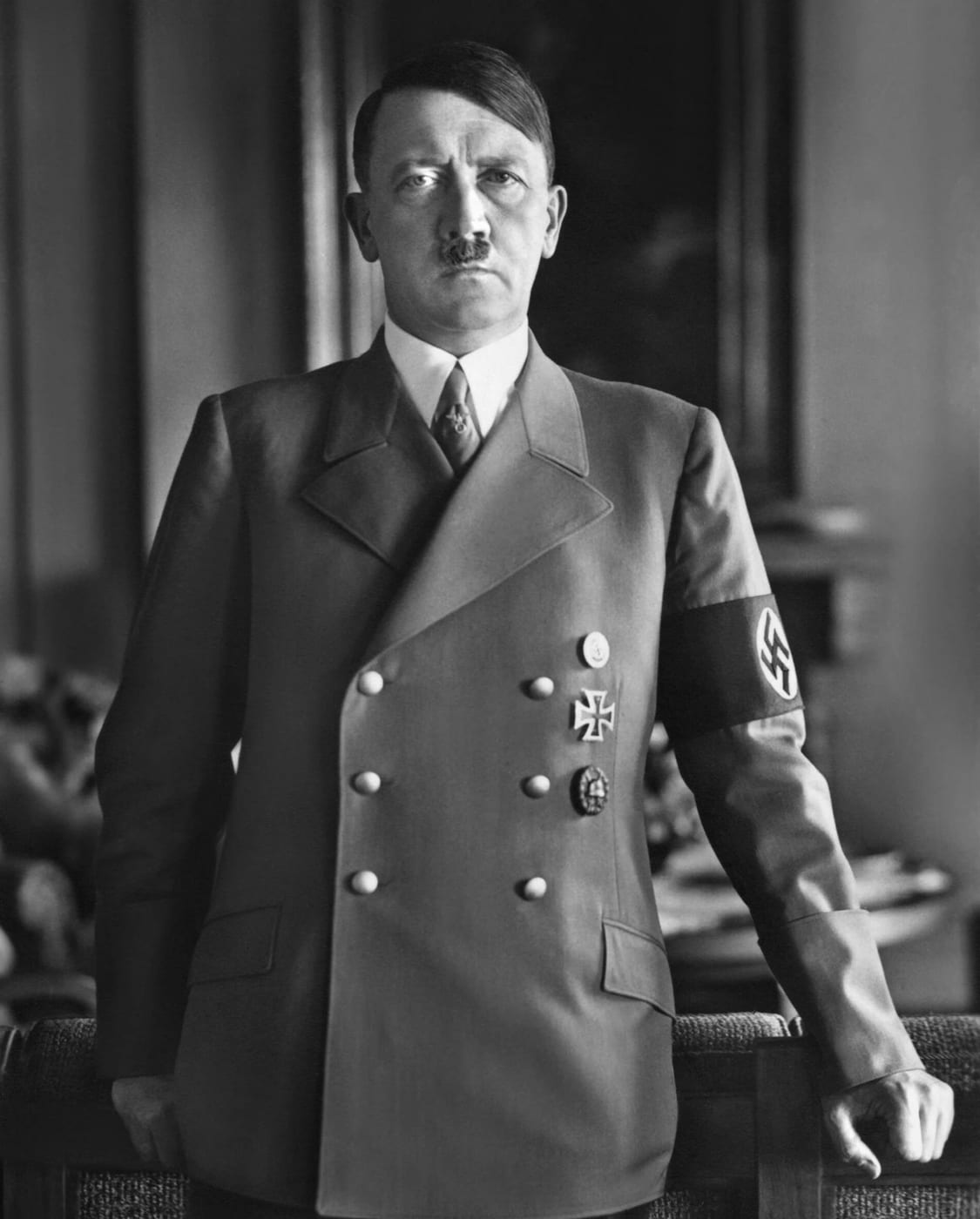 Black-and-white portrait of Adolf Hitler standing in a double-breasted uniform jacket and armband.