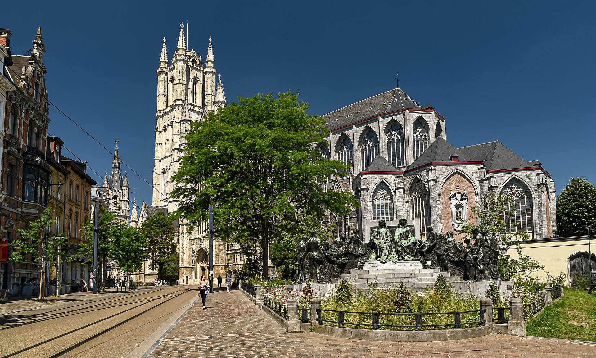 Saint Bavo’s Cathedral tower rises above trees and the bronze monument to the van Eyck brothers.